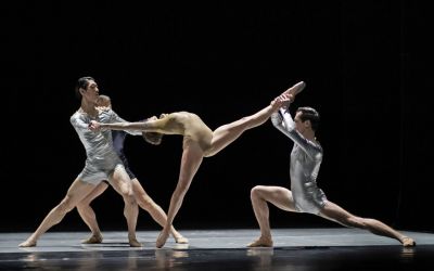 trzech tancerzy w czarnych oraz srebrnych trykotach trzymają kobietę w kremowym trykocie za nogę oraz ręce, kobieta jest wygięta, stoi na jednej nodze, drugą ma uniesioną bardzo wysoko